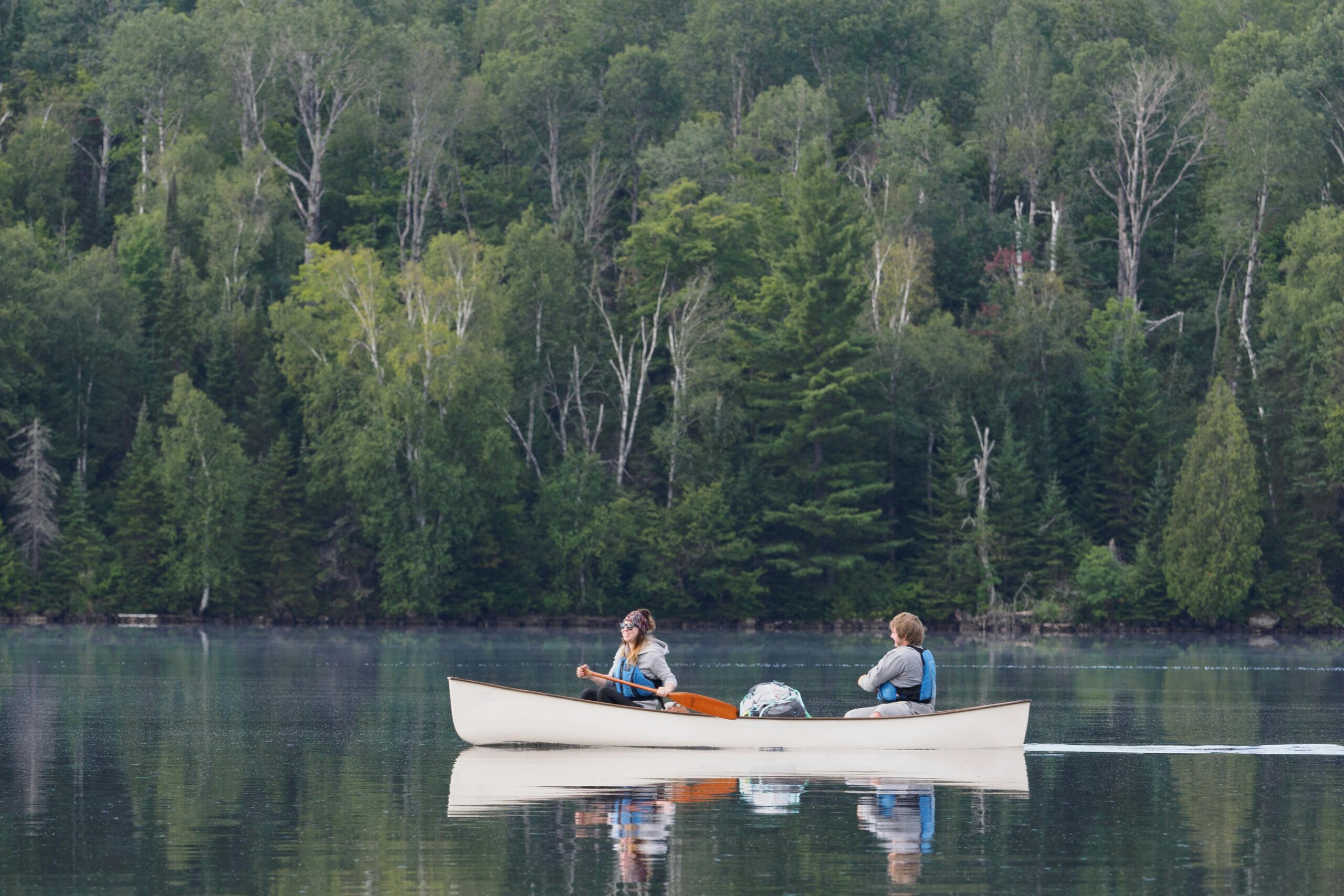 Two people kayaking in a tranquil lake, surrounded by lush forest, reflecting nature's beauty.