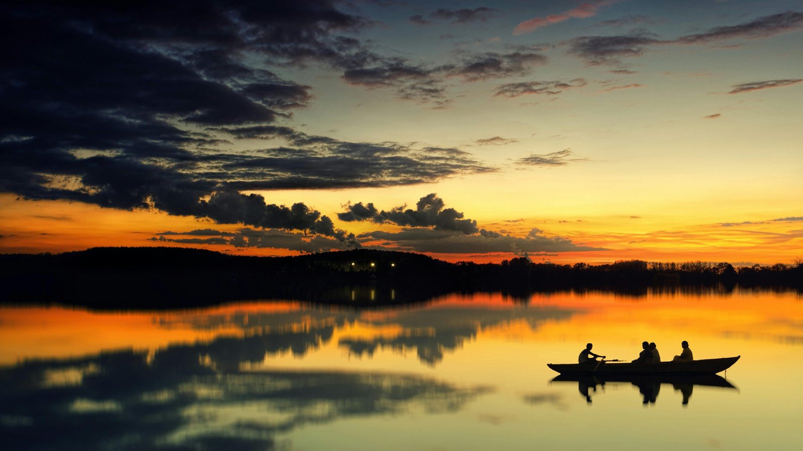 Silhouetted fishermen in a boat on a tranquil lake during sunrise. Perfect reflection.