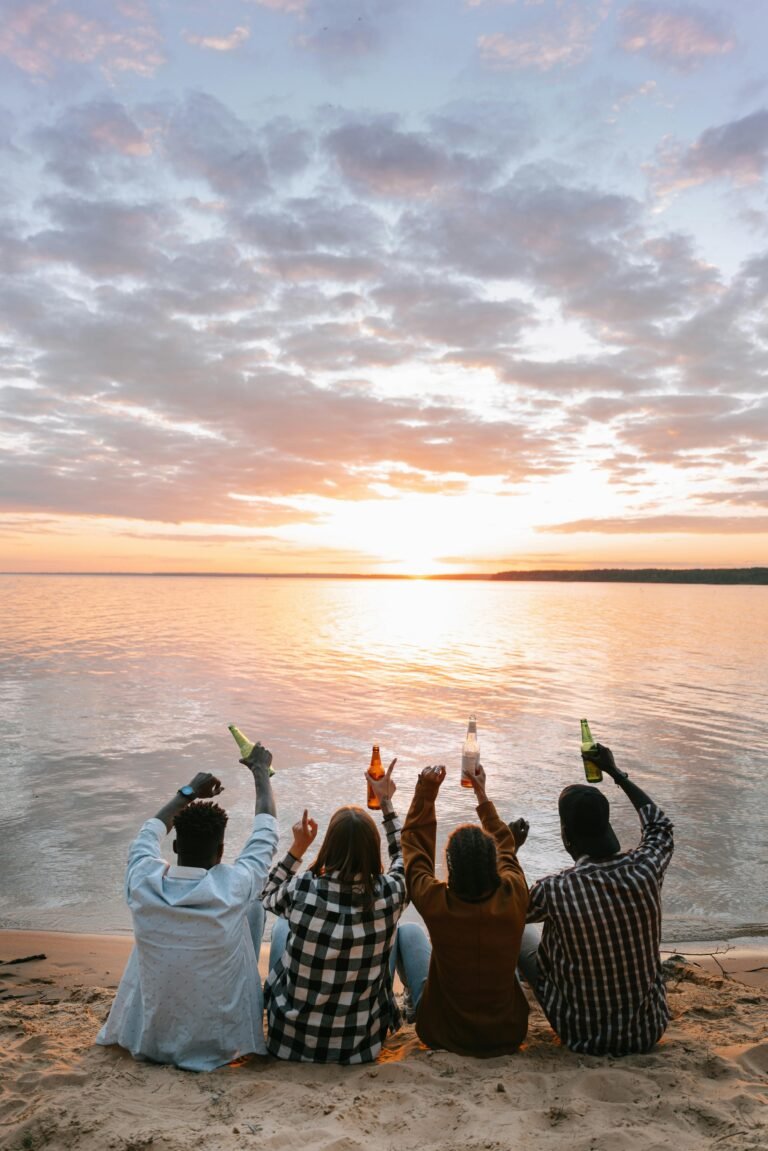 Four friends sitting by the beach enjoying drinks at sunset.